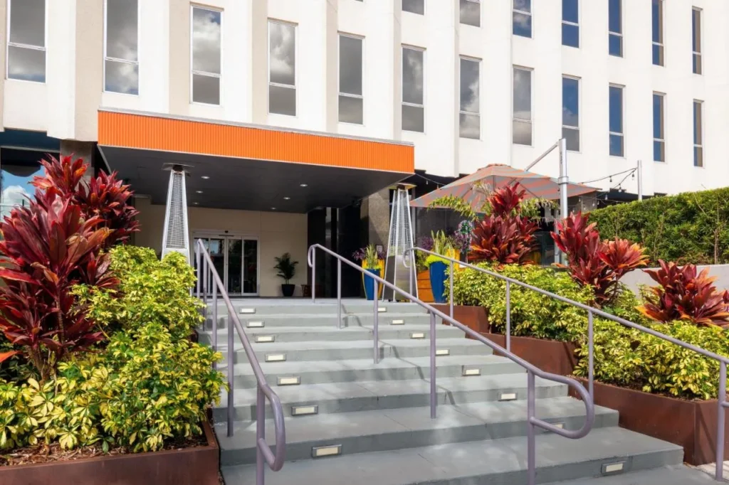 Escaleras de entrada bordeadas de plantas rojas y verdes debajo del dosel naranja en Aloft Orlando Downtown