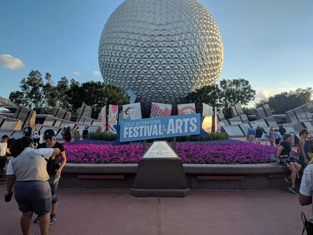 EPCOT International Festival of the Arts sign and purple flower bed in front of Spaceship Earth