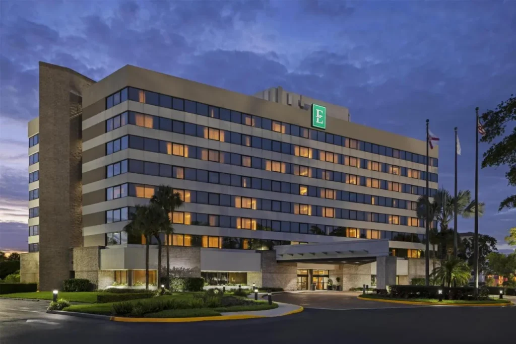 Exterior at dusk with lit windows and palm trees at Embassy Suites Orlando International Drive ICON Park