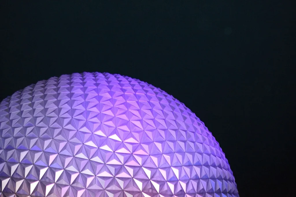 Faceted dome of Spaceship Earth glowing purple against the night sky at EPCOT