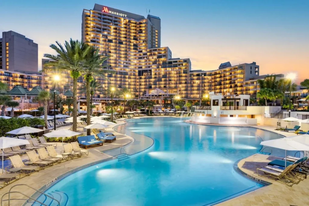 Laguna Falls Pool con tumbonas y sombrillas debajo de la torre iluminada Orlando World Center Marriott