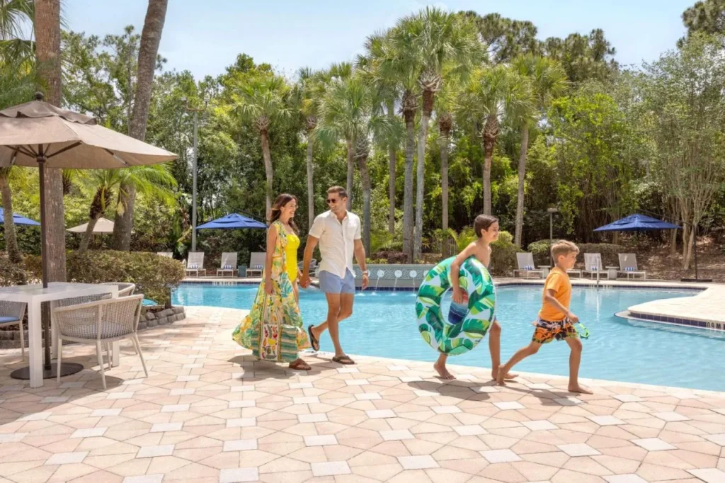 Family with pool floats beside the palm-lined pool at DoubleTree Suites Disney Springs