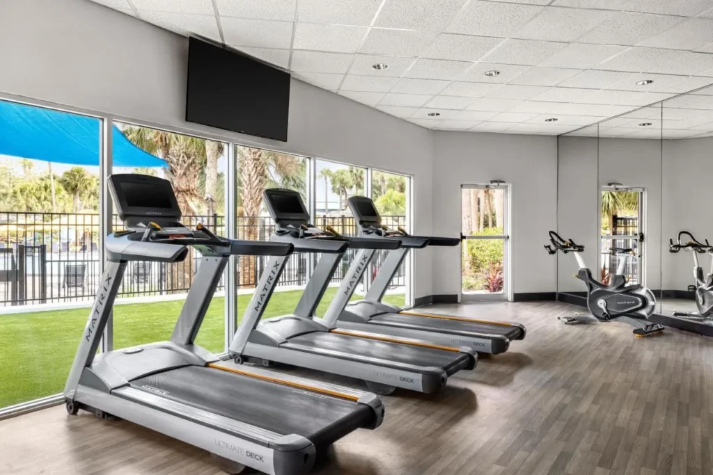 Gimnasio con cintas de correr y bicicletas est&aacute;ticas frente al c&eacute;sped en Delta Hotels Orlando Celebration