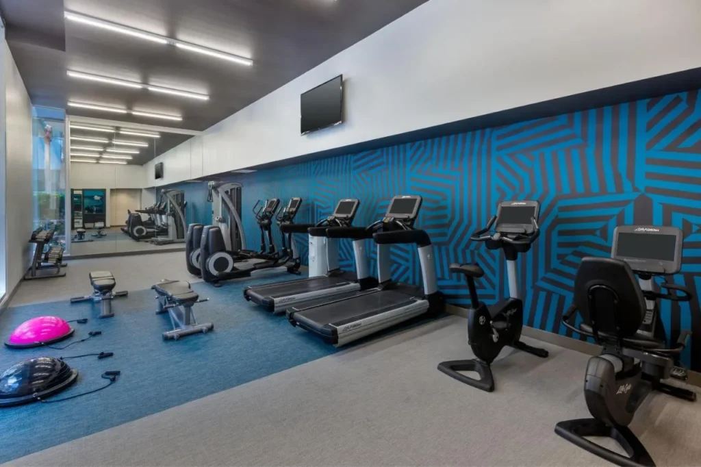 Gimnasio con cintas de correr, bicicletas estáticas y una pared con motivos azules en el Aloft Orlando Downtown