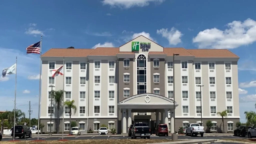 Five-story exterior with flags and parking lot at Holiday Inn Express & Suites Orlando South-Davenport
