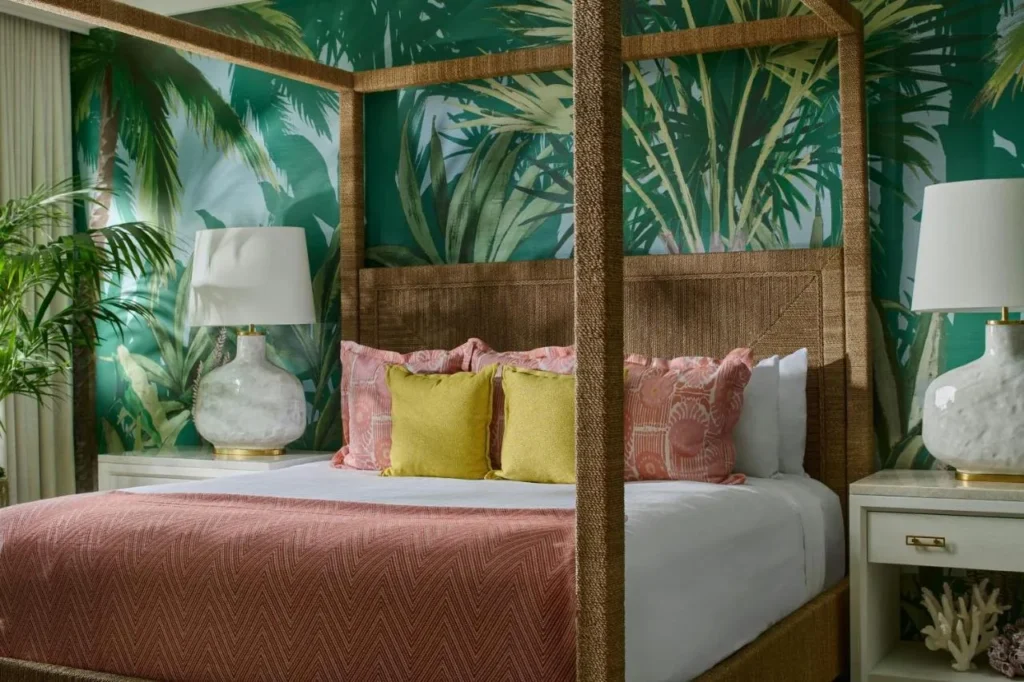 Four-poster bed with a coral bedspread and palm-print wallpaper in a Gaylord Palms guest room