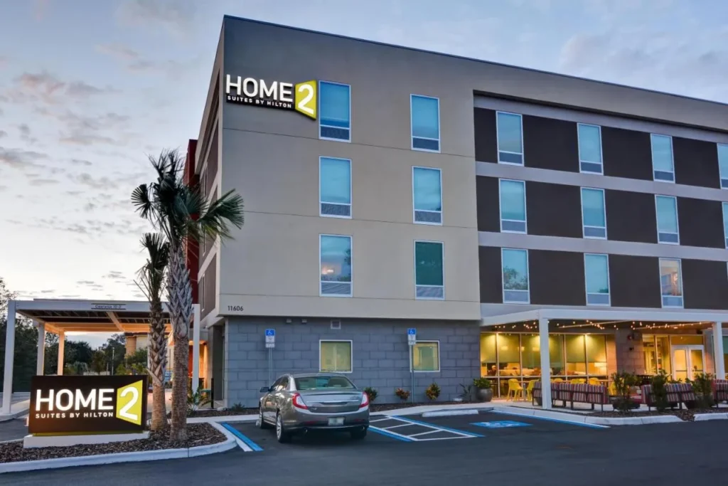 Exterior de cuatro pisos con palmeras y patio iluminado en Home2 Suites by Hilton Tampa USF