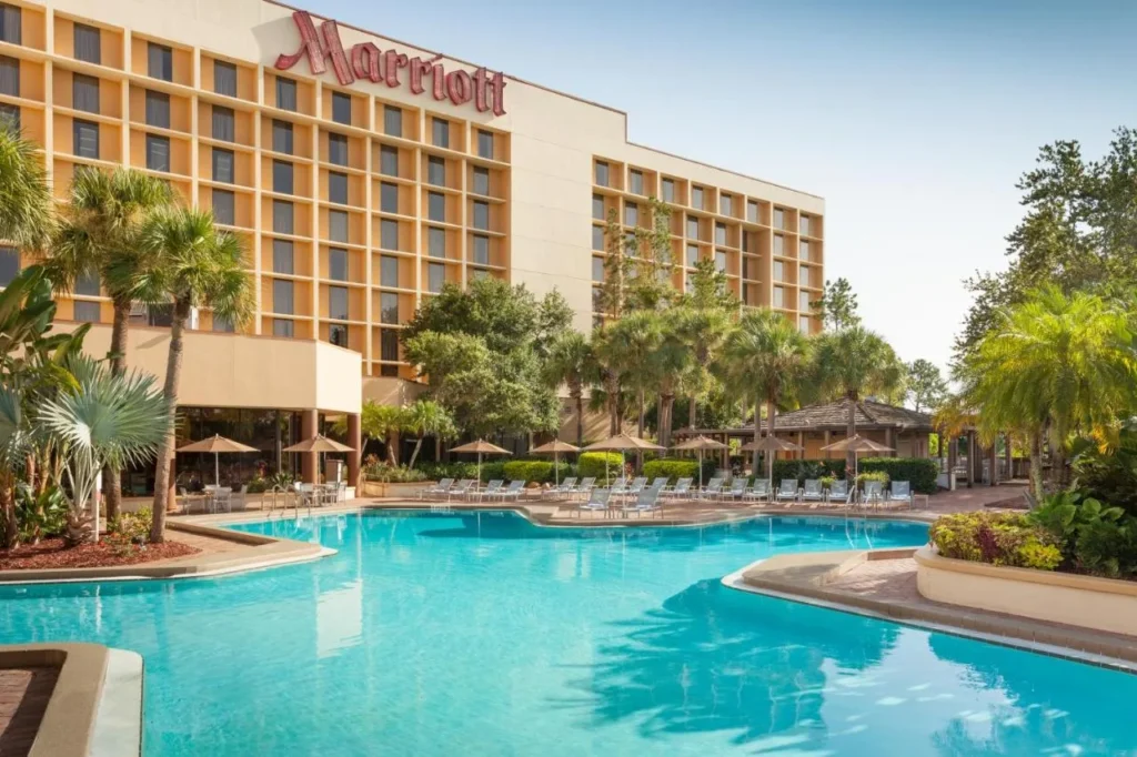 Piscina exterior de forma libre con tumbonas y palmeras debajo de la torre Marriott Orlando Airport Lakeside