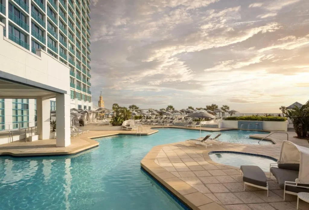 Free-form pool and hot tub beside the tower of Hilton Daytona Beach Oceanfront Resort at sunset