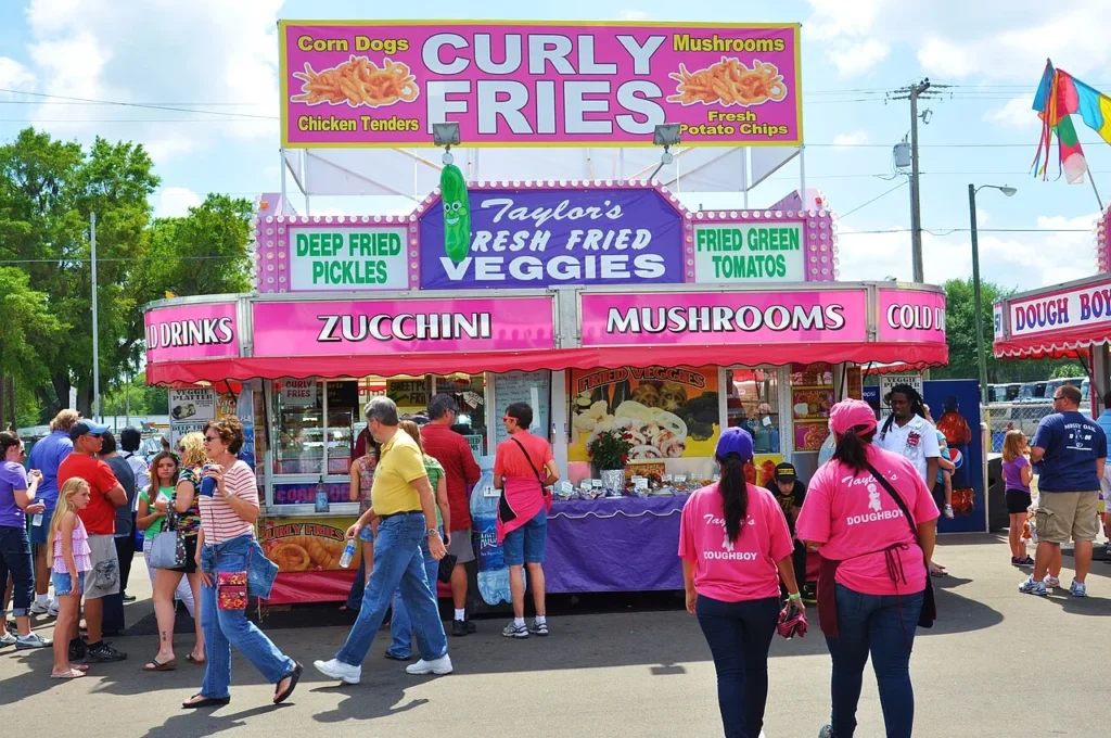 Fried food stand with pink signs and visitors at the Florida Strawberry Festival in Plant City