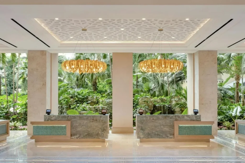 Recepci&oacute;n con mostradores de m&aacute;rmol y l&aacute;mparas de oro frente a un jard&iacute;n tropical en Gaylord Palms Resort