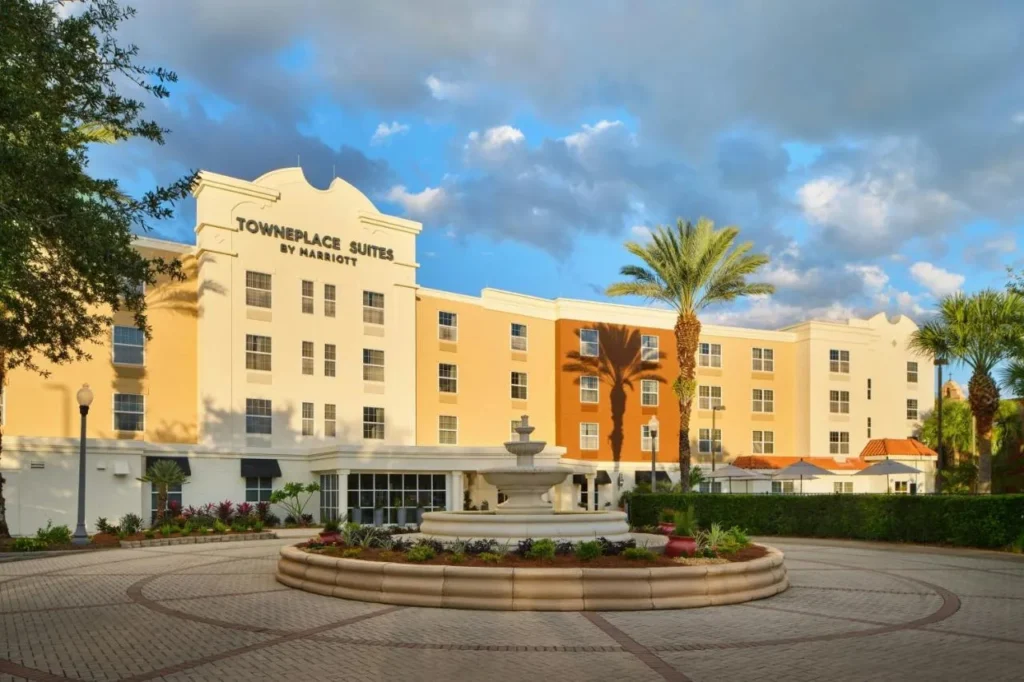 Frente a TownePlace Suites The Villages con una fuente, palmeras y un c&iacute;rculo de entrada pavimentado con ladrillos