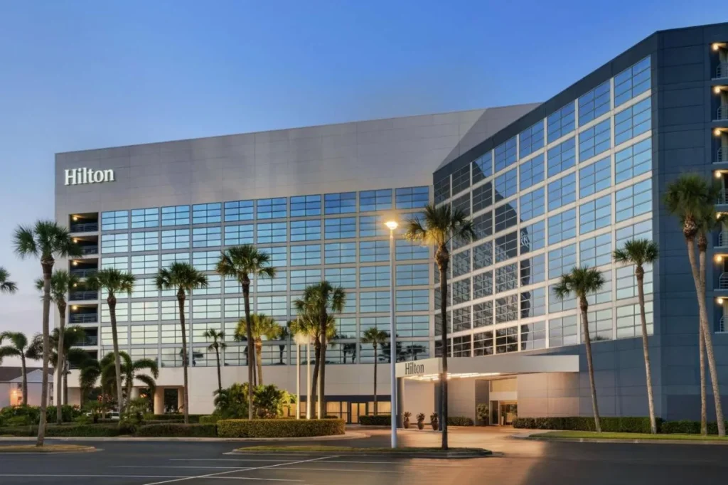 Glass facade and palm-lined entrance of Hilton Melbourne, FL at Rialto Place at dusk