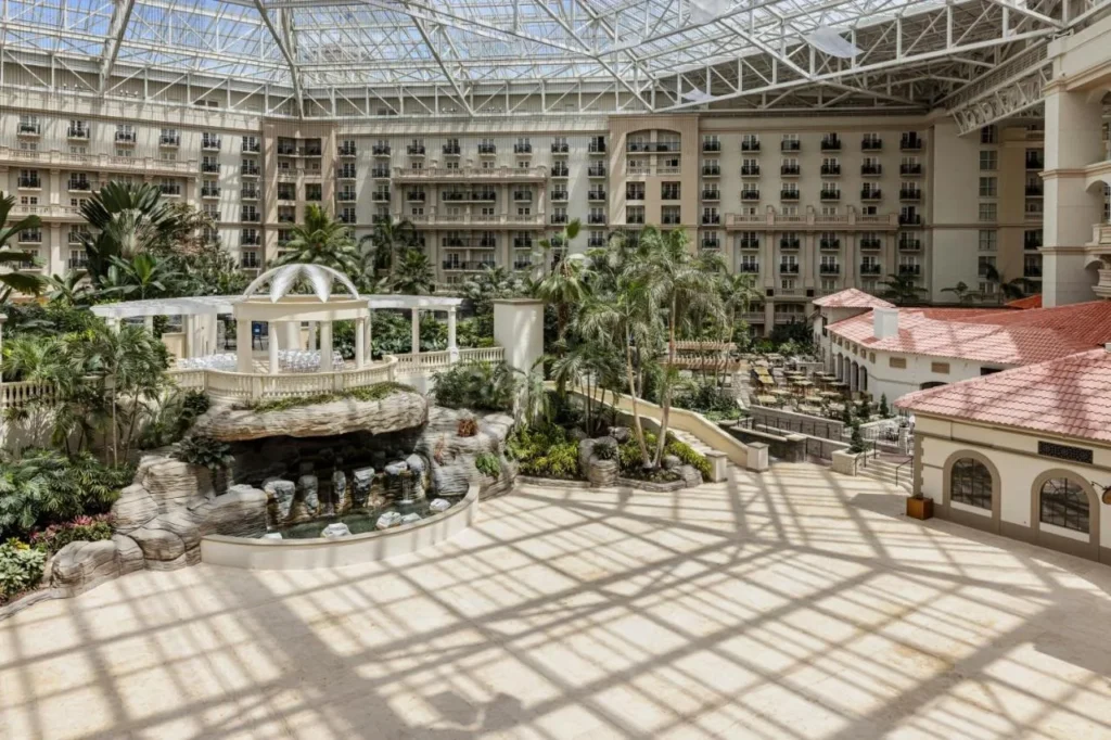 Atrio con techo de vidrio con mirador, cascada de roca y palmeras en Gaylord Palms Resort