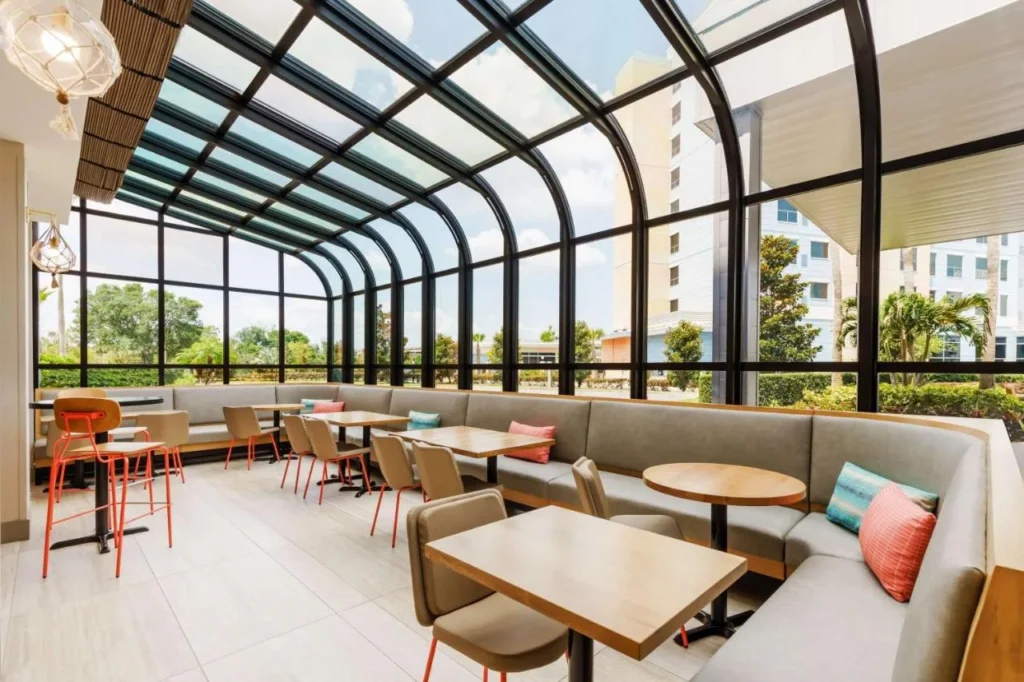 Área de asientos con techo de vidrio con cabinas y mesas en Hyatt Place across from Universal Orlando