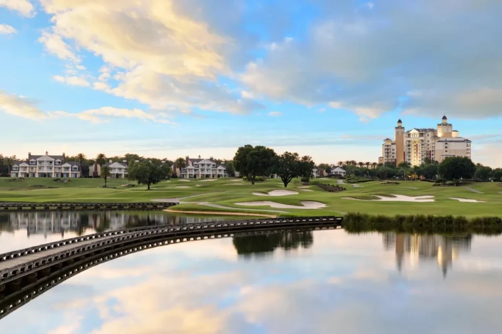 Golf course lake with a curved wooden bridge, villas and the Reunion Grande tower beyond