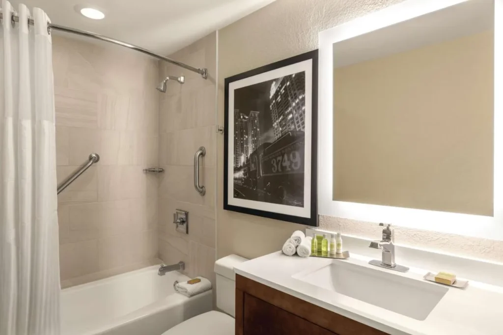 Ba&ntilde;o de invitados con ba&ntilde;era-ducha, barras de apoyo y un espejo retroiluminado en DoubleTree by Hilton Orlando Downtown