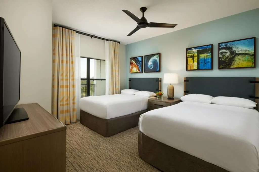 Habitaci&oacute;n de invitados con dos camas, ventilador de techo y puerta de balc&oacute;n en una villa Sheraton Vistana Villages