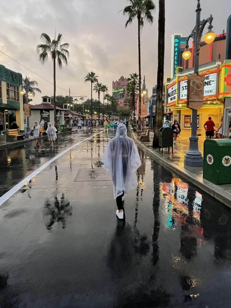 Invitado con un poncho claro caminando por un Hollywood Boulevard empapado de lluvia en Disney's Hollywood Studios