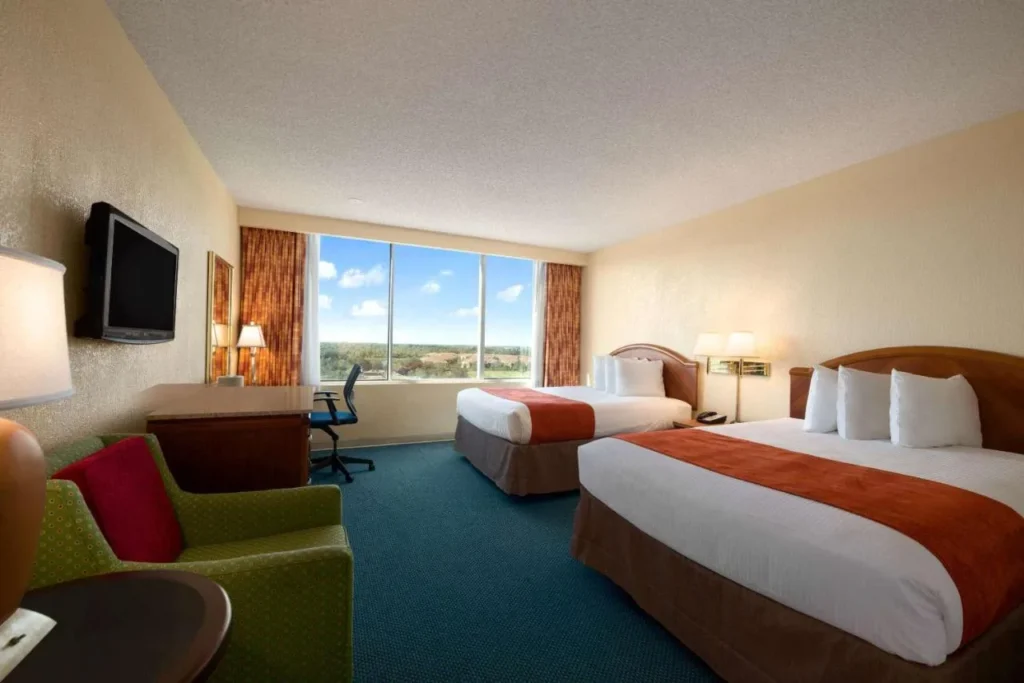 Habitación con dos camas, sillón y ventana grande en Ramada by Wyndham Kissimmee Gateway