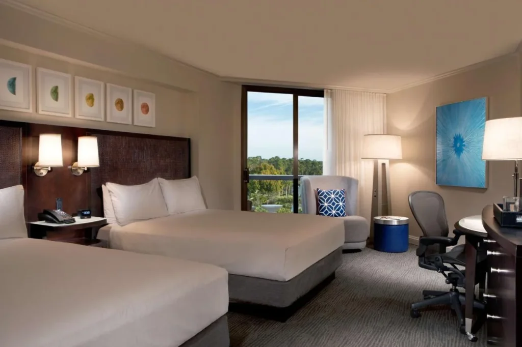 Habitación con dos camas, sillón, escritorio y puerta de balcón en Hilton Orlando Buena Vista Palace