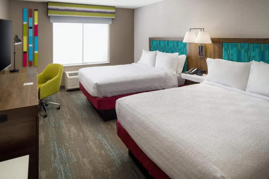 Habitación con dos camas, escritorio y silla verde en el Hampton Inn Kissimmee North