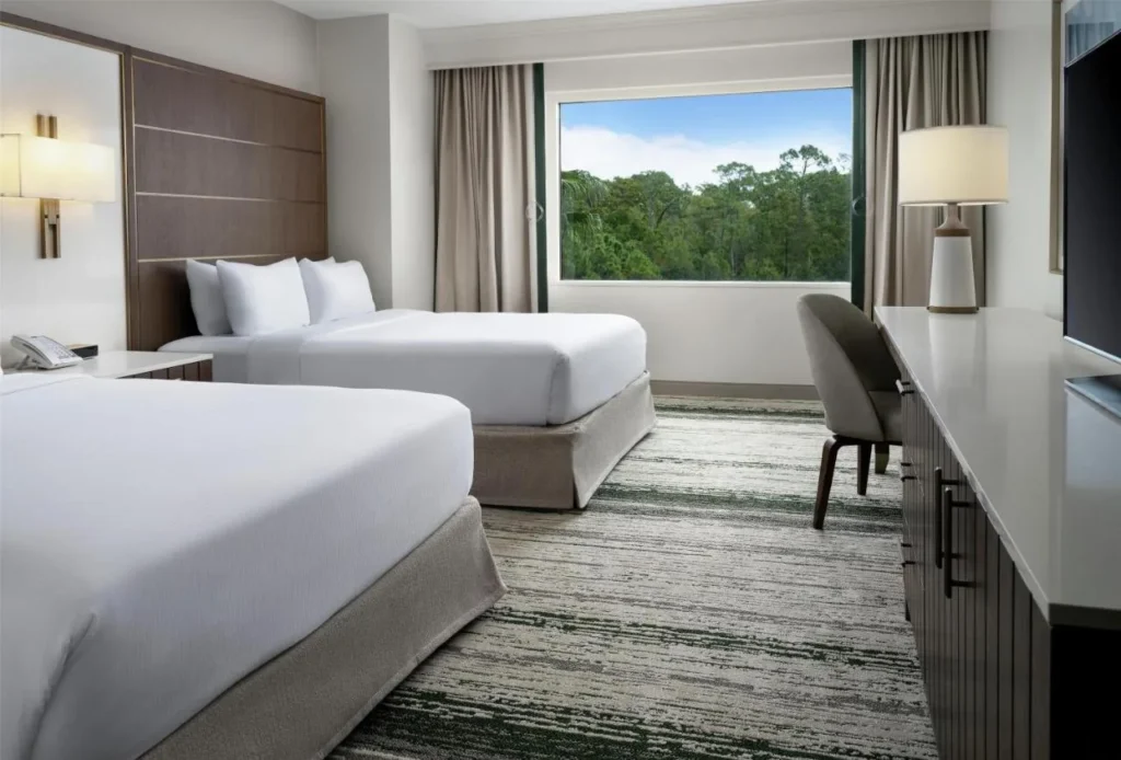 Habitación con dos camas, escritorio y ventana amplia sobre árboles en Signia by Hilton Orlando