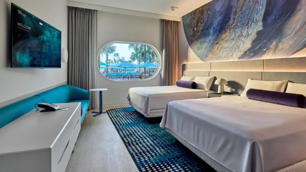 Habitación con dos camas, TV de pared y ventana ovalada en Universal's Terra Luna Resort