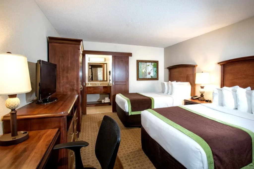 Habitación con dos camas, cabeceros de madera, escritorio y TV en Rosen Inn Lake Buena Vista