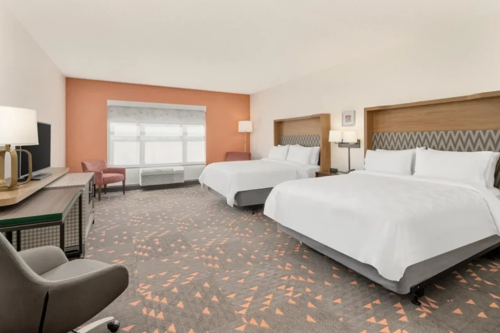 Habitaci&oacute;n con dos camas queen, una pared con acento naranja y un escritorio en Holiday Inn & Suites Orlando I-Drive