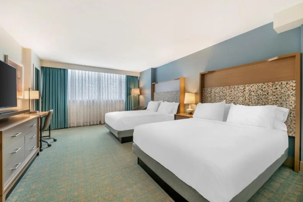 Habitación con dos camas queen y cortinas de verde azulado en el Holiday Inn Orlando Disney Springs Área