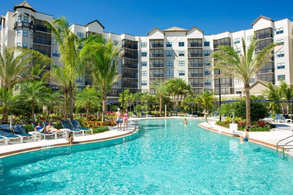 Los hu&eacute;spedes se relajan alrededor de una piscina con palmeras debajo de las torres de la suite de The Grove Resort & Water Park Orlando