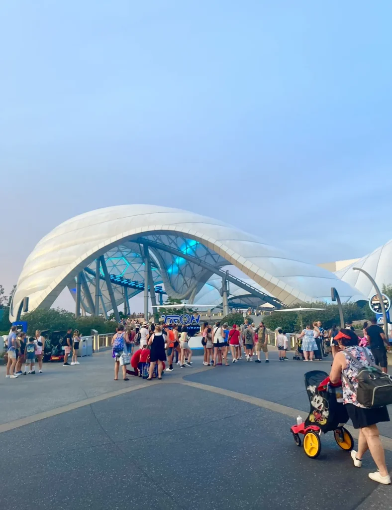 Guests walking toward the white canopy of TRON Lightcycle / Run at Magic Kingdom at dusk