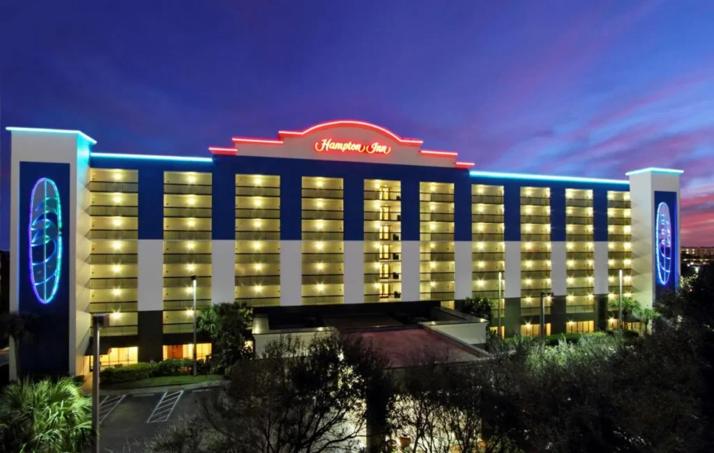 Hampton Inn Cocoa Beach building lit up at dusk with neon trim and rows of balconies