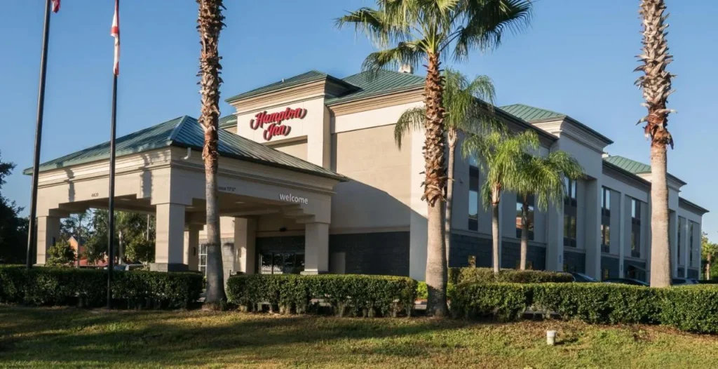 Hampton Inn Lakeland entrada con su dosel de bienvenida, techo verde y altas palmeras