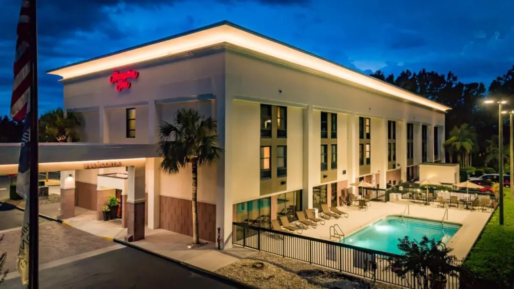 Hampton Inn Mount Dora exterior at dusk with lit outdoor pool and lounge chairs
