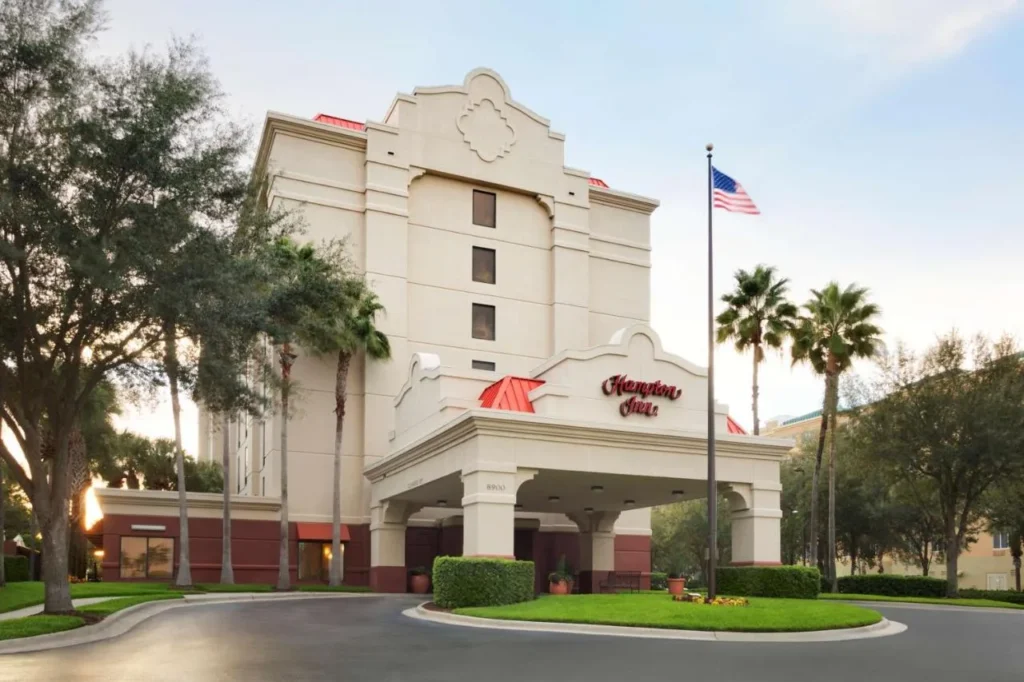 Hampton Inn Orlando International Drive/Convention Center entrada con porte-cochere, asta de bandera y palmeras