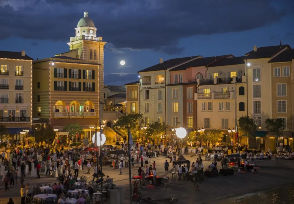 Harbor Piazza por la noche con una torre de reloj iluminada y multitudes en Loews Portofino Bay