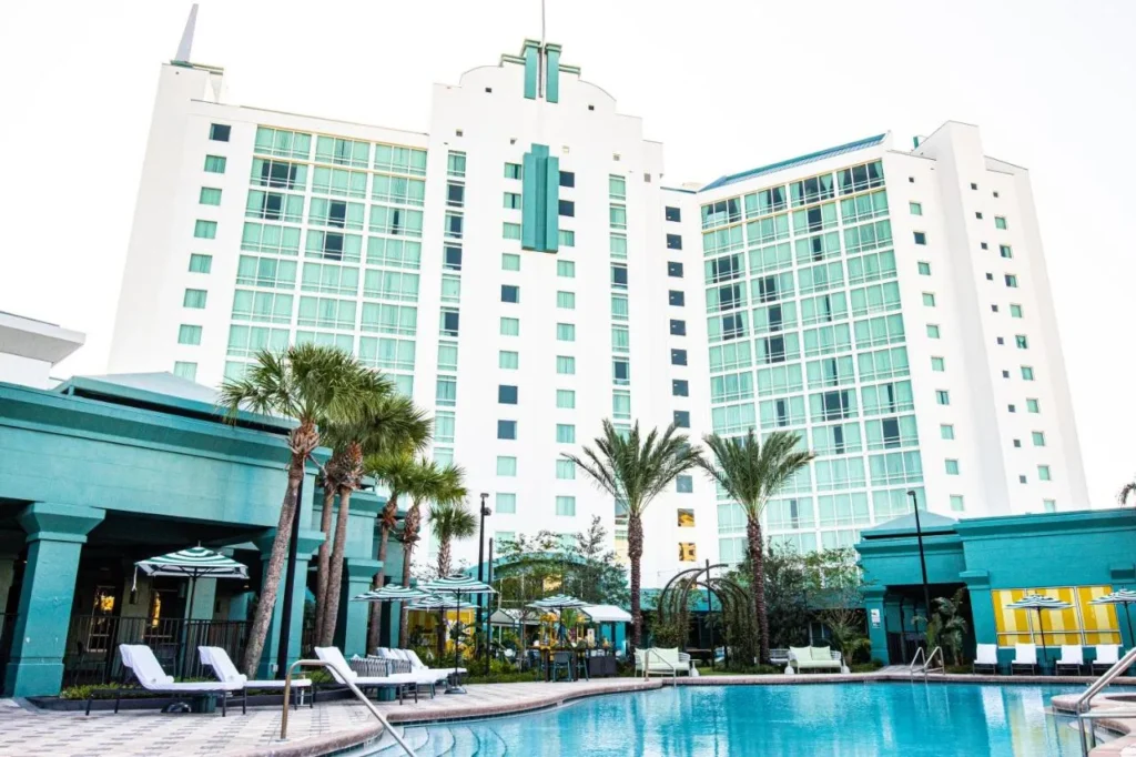 Piscina climatizada con tumbonas y sombrillas debajo de la torre blanca del Hotel Landy Orlando