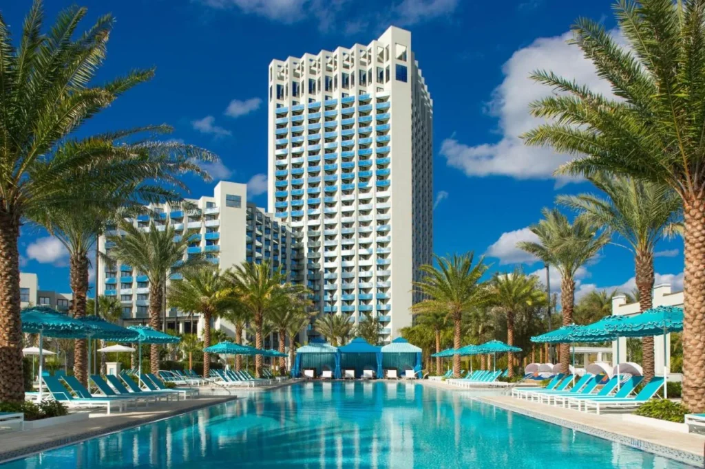Torre Hilton Orlando Buena Vista Palace sobre la piscina bordeada de palmeras con tumbonas y caba&ntilde;as turquesas