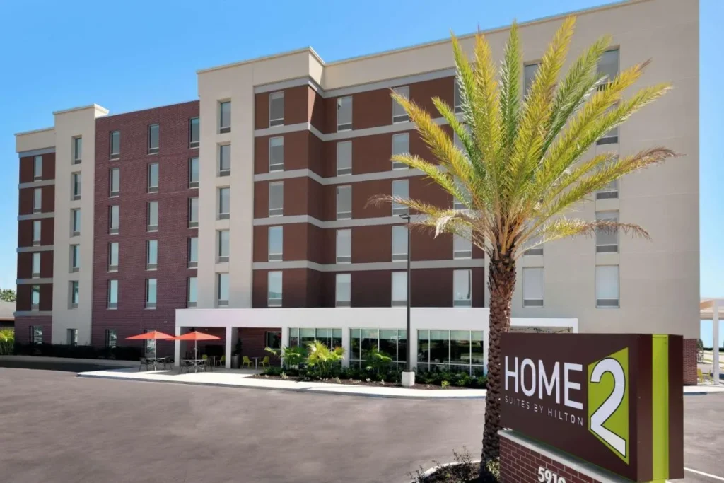 Home2 Suites by Hilton Orlando Near Universal building, palm tree, sign and parking area
