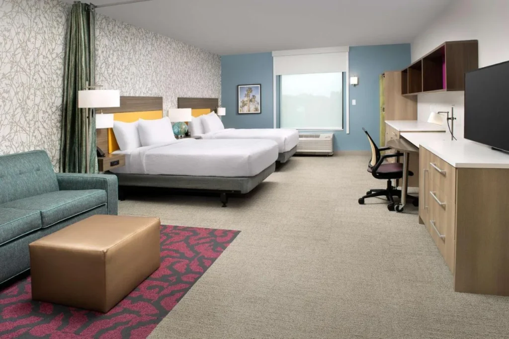 Home2 Suites Orlando Downtown estudio con dos camas, un sofá, escritorio largo y estanterías de pared