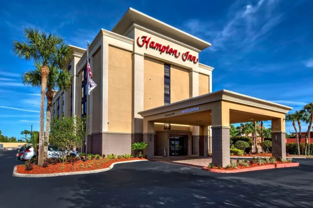 Hotel entrance with palm trees and covered drive at Hampton Inn Orlando-Maingate South in Davenport