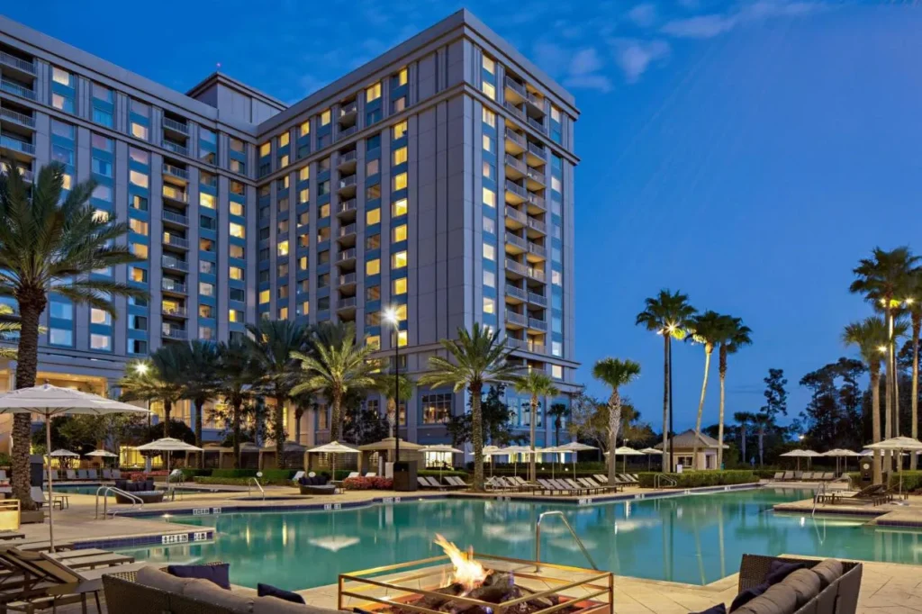 Torre del hotel y piscina bordeada de palmeras con fogata al atardecer en Waldorf Astoria Orlando