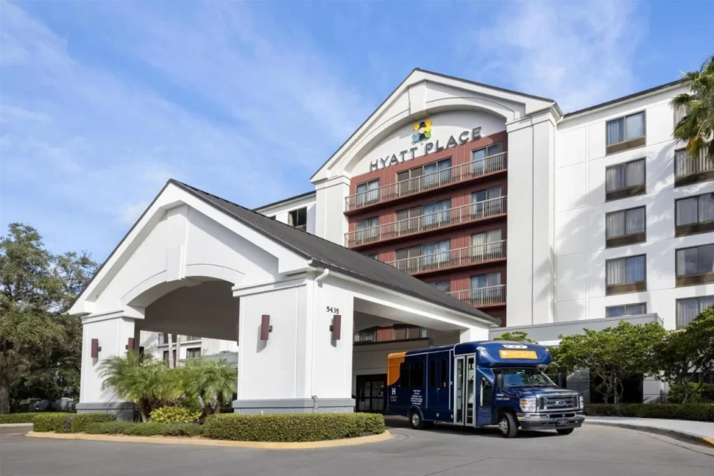 Entrada al Hyatt Place Orlando Airport con un autob&uacute;s de enlace de hotel azul bajo el porte-cochere