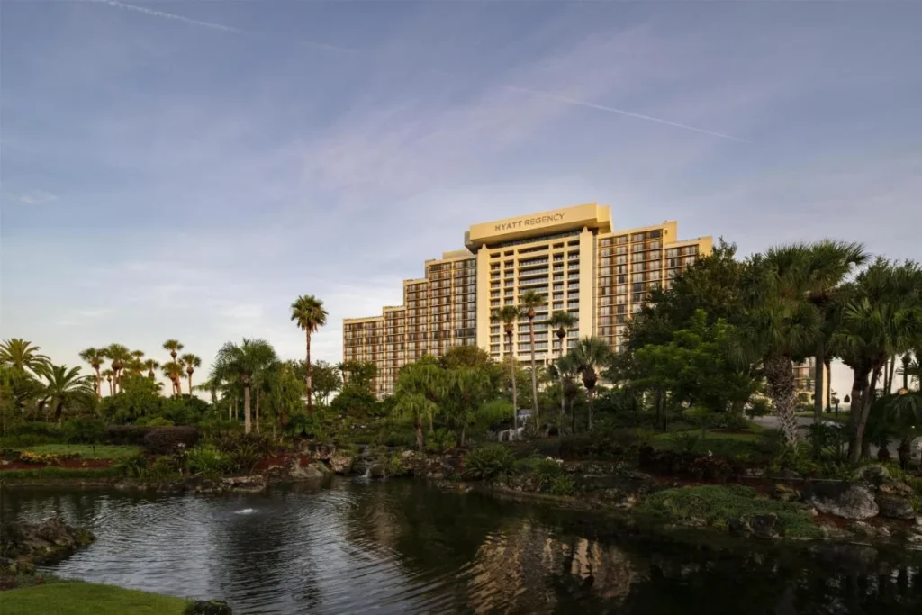 Hyatt Regency Grand Cypress tower above palm trees and a pond under a pastel sky