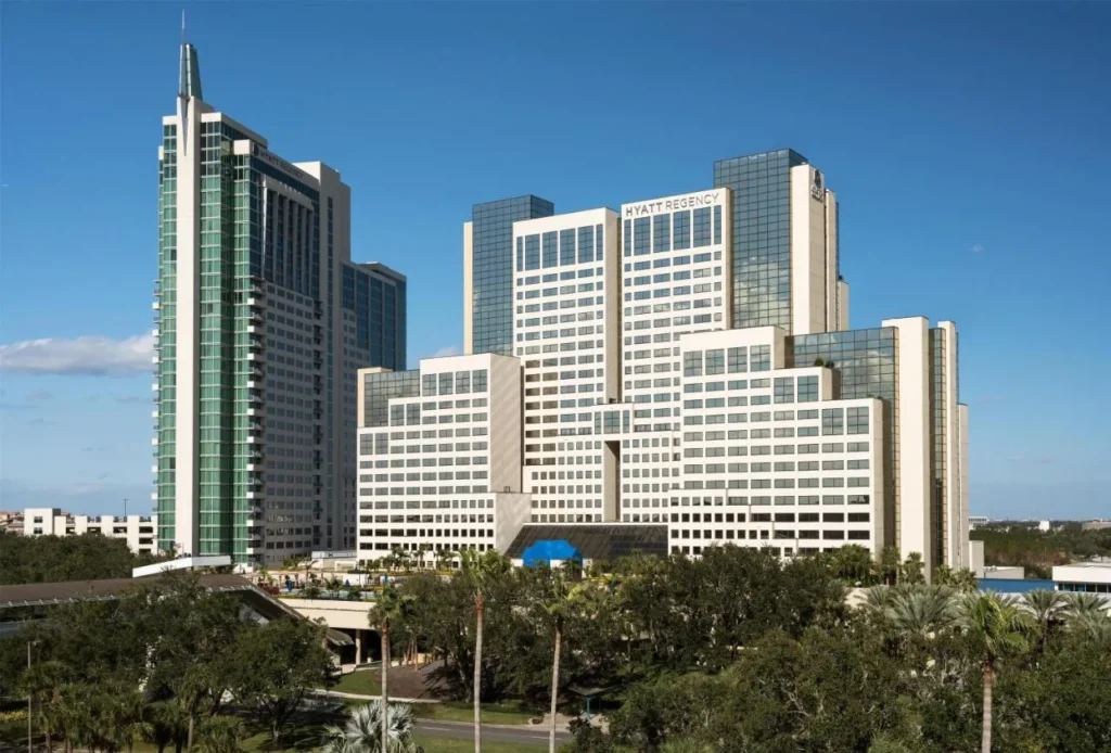 Las dos torres del hotel Hyatt Regency Orlando se elevan sobre robles y palmeras bajo un cielo azul