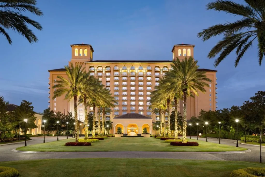 Fachada iluminada y c&eacute;sped de entrada bordeado de palmeras al atardecer en The Ritz-Carlton Orlando, Grande Lakes
