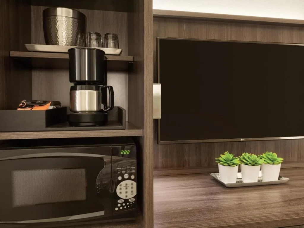 Cafetera, vasos y microondas junto al gabinete de TV en Buena Vista Suites