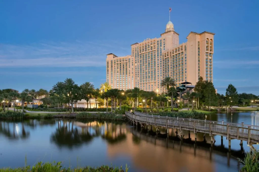 JW Marriott Orlando Grande Lakes torre al atardecer sobre un lago, paseo marítimo y torre de tobogán de agua